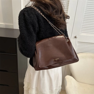 Minimalist dark brown leather tote bag with gold chain strap on a female model