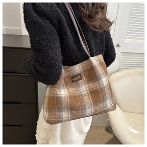 Close-up of brown plaid wool tote bag featuring a leather logo patch and thin straps