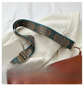 Detail of bohemian patterned shoulder strap with golden metal buckles on brown leather bag