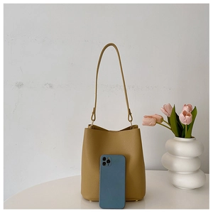 Detail of yellow pebbled leather bucket bag shown with a smartphone for size reference