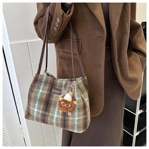 Detail of wool plaid bucket bag with plush lion charm and brown leather straps