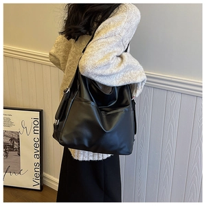 Side view of large black PU tote bag worn by a model in a minimalist interior setting