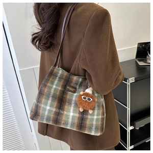 Detail of wool plaid tote bag featuring brown leather strap and fuzzy pompom charm