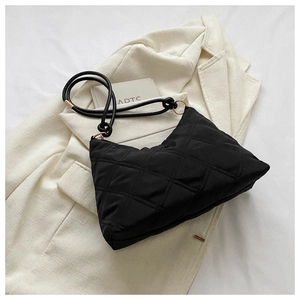 Close-up of black quilted puffer shoulder bag on a beige blazer background
