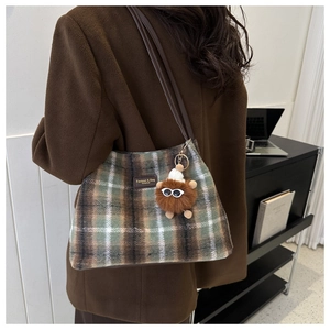 Detail of plaid shoulder bag featuring a fuzzy monster charm and leather brand label