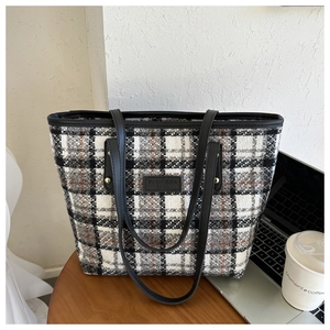 Detailaufnahme einer schwarz-weißen Tweed-Tragetasche mit Ledergriffen auf einem Tisch