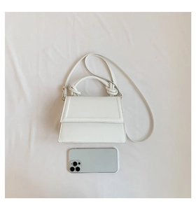 Sac à main blanc avec poignée nouée à côté d'un téléphone pour l'échelle de taille