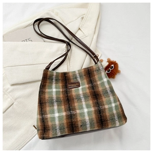 Close-up of wool plaid shoulder bag with leather logo tag and plush charm detail