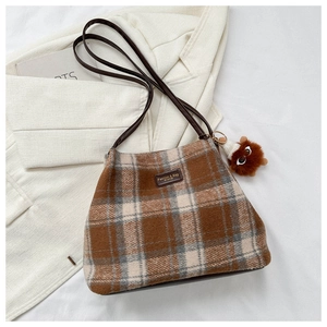 Close-up of wool plaid tote bag with brown leather strap and plush doll charm