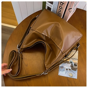 Detail of a brown leather half-moon bag with adjustable fabric strap on a wooden table
