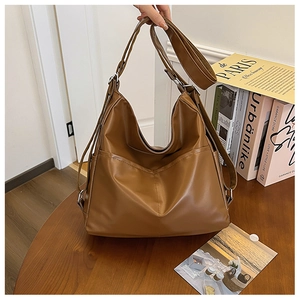 Detailed view of caramel brown faux leather tote bag on wooden surface with art books