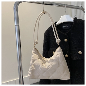 Detail of cream quilted shoulder bag with knotted strap against black tweed jacket