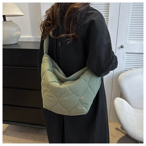 Detailed side view of bean green quilted puffer bag worn by model in a modern room