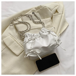 Detail der weißen Plissee-Tasche mit Schleifen und silbernem Kettenriemen auf Blazer