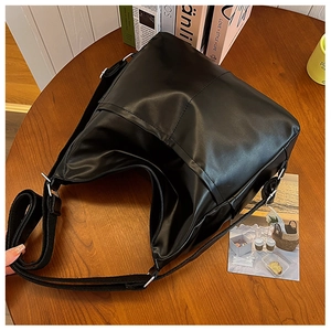 Detail of black glossy PU leather tote bag with adjustable strap on a wooden table