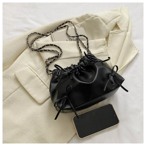 Draufsicht der schwarzen Falten-Eimertasche mit Schleifen und Silberkette auf beigem Blazer