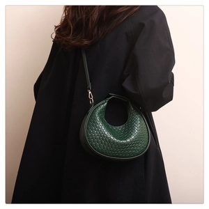 Close-up of dark green woven crescent shoulder bag on model with detailed texture