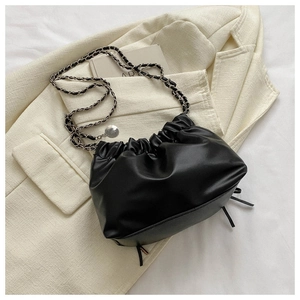 Detail der schwarzen Rafftasche mit geflochtener Silberkette auf beigem Blazer
