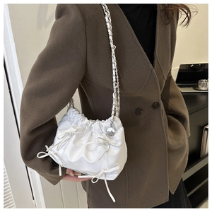 Detail der weißen Plissee-Beuteltasche mit Schleifen und silberner Kette am Model