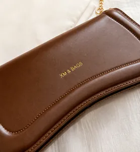 Detail of brown leather bag with golden chain and visible logo on cream fabric