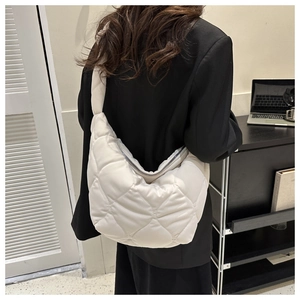 Quilted beige puffer tote bag with diamond pattern shown on a shoulder over a black blazer