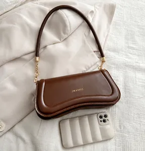 Close-up of brown leather underarm bag with gold chain strap and XM & BAGS logo detail