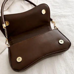 Detail of golden magnetic snap closure and chain connection on dark brown leather bag