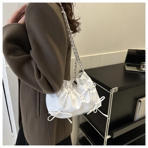 Détail d'un sac plissé blanc avec des nœuds décoratifs et une bandoulière en chaîne