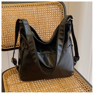 Close-up of a large black faux leather tote bag with wide straps on a rattan chair