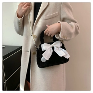 Détail d'un sac à main en peluche noire avec nœud blanc géant et bandoulière en perles