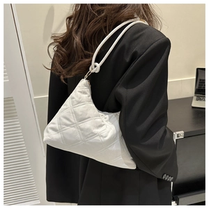 Close-up of white quilted shoulder bag with knot detail held by a model in office