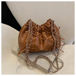 Detail der braunen Falten-Beuteltasche mit dekorativen Lederschleifen und Metallketten