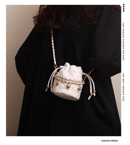 Detail of white quilted bucket bag with gold heart charm and chain strap on model
