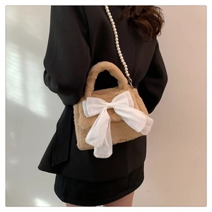 Detail of khaki plush crossbody bag featuring a large white bow and pearl chain strap