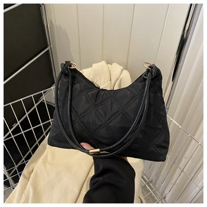 Detail of black quilted shoulder bag with gold hardware held over a white basket