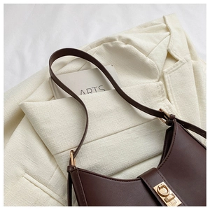 Détail du sac sous le bras en cuir marron foncé avec boucle dorée sur un blazer beige