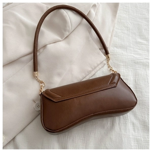 Close-up of brown PU leather underarm bag with gold chain strap on beige fabric
