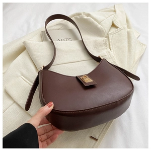 Détail d'un sac hobo marron foncé avec boucle dorée posé sur un blazer de couleur neutre