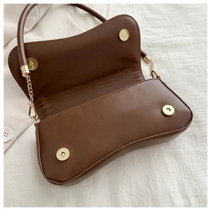 Detail of the brown baguette bag with dual gold magnetic clasps and crescent leather shape