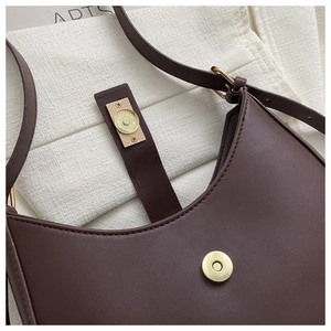 Gros plan sur le fermoir magnétique doré et le cuir mat marron foncé du sac sous le bras