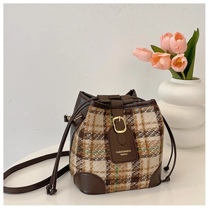 Detail of retro plaid bucket bag with brown leather trim and golden buckle closure