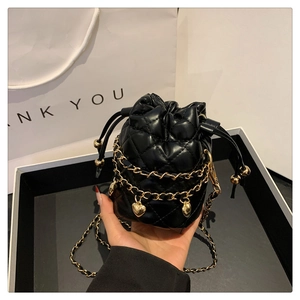 Detail of quilted bucket bag with gold chain edge and heart-shaped metal pendant charm