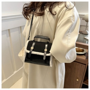 Detail of a black leather crossbody bag with white faux fur trim and gold metal buckles