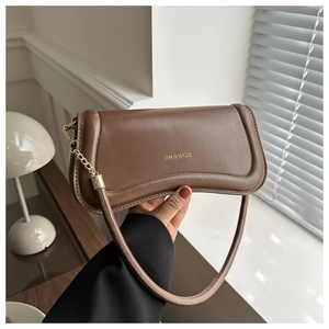 Detail of a brown leather shoulder bag with gold metal chain and XM BAGS logo by the window