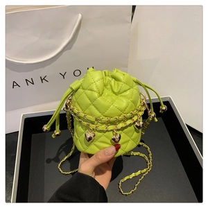 Close-up of vibrant green quilted bucket bag with gold heart pendant and chain strap