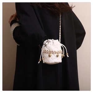 Detail of white quilted bucket bag with gold heart charms and chain strap on black coat