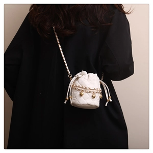 White quilted bucket bag with gold heart charms and chain strap shown on a model