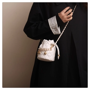 Detail of white quilted bucket bag with gold chain and heart-shaped metal charms