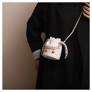 Detail of white quilted bucket bag with gold heart charms worn by model on black coat