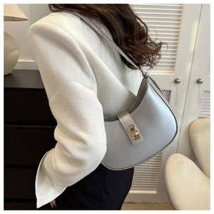 Sac bandoulière demi-lune gris clair avec boucle dorée sur un blazer blanc élégant